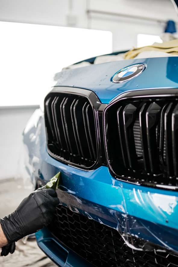 Paint protection film (PPF) being applied to front bumper of blue BMW M2C