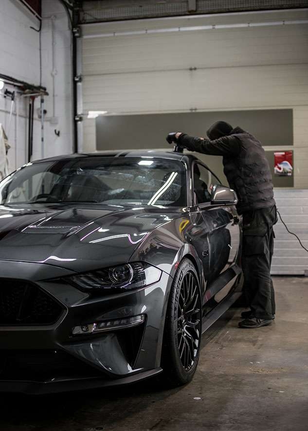 Man in gloves polishing Grey Mustang GT with machine