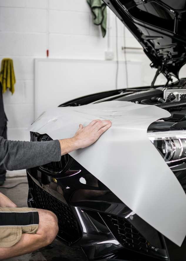 Paint protection film (PPF) being applied to front bumper of black BMW M2C