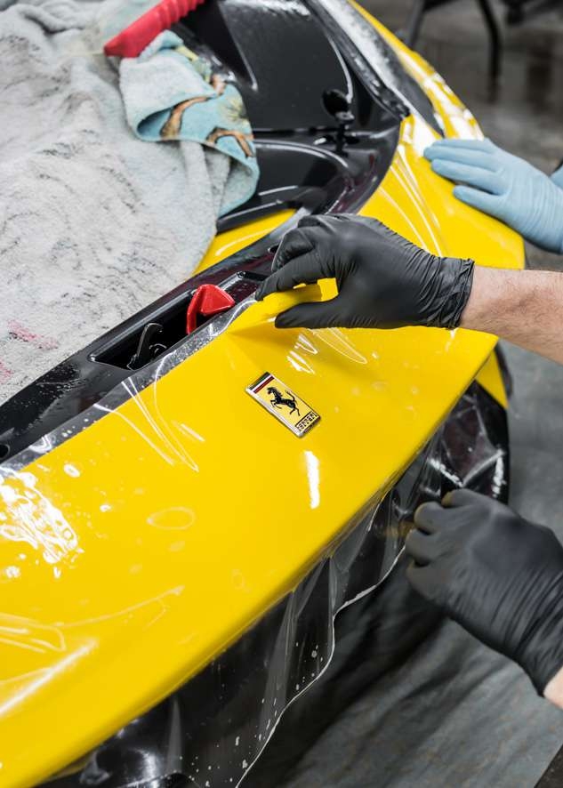 Paint protection film (PPF) being applied to yellow Ferrari 488 Pista badge and front bumper