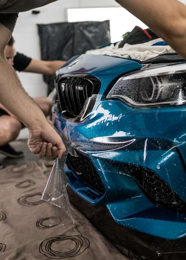 Paint protection film (PPF) being applied to front bumper of blue BMW M2C